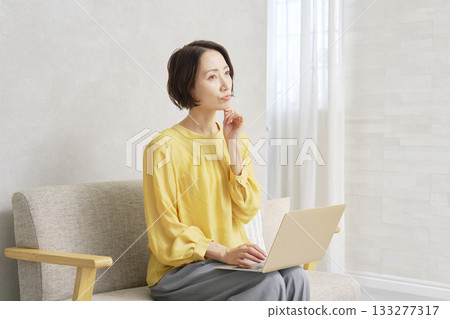 A woman using a computer in the living room thinking 133277317