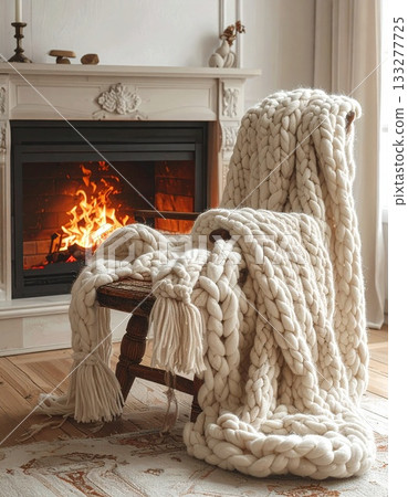 A warm-looking knitted blanket draped over a chair by the fireplace A warm-looking knitted blanket draped over a chair by the fireplace 133277725