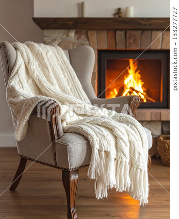A warm-looking knitted blanket draped over a chair by the fireplace A warm-looking knitted blanket draped over a chair by the fireplace 133277727