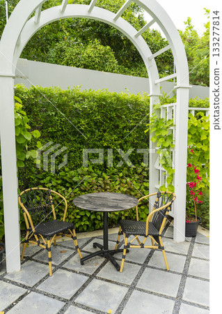 Wooden chairs and table in a beautiful garden canopy in home landscaped garden in summer. Wooden chairs and table in a beautiful garden canopy in home landscaped garden in summer. 133277814