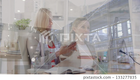 Collaborating colleagues wearing blazers discussing report at office, with smartphone and notebook Collaborating colleagues wearing blazers discussing report at office, with smartphone and notebook 133277835