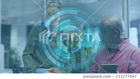 Woman wearing knit sweater and senior man reviewing data overlay at desk in office, holding tablet 133277847