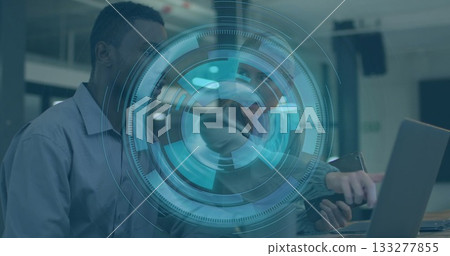 Coworkers wearing business casual attire working on laptop in office, with smartphone, data overlay 133277855