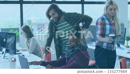 Collaborating four colleagues typing and pointing at monitors in open-plan office, with coffee cups 133277989