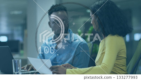 Woman in yellow blazer holding report, man typing on laptop at office desk with holographic overlay Woman in yellow blazer holding report, man typing on laptop at office desk with holographic overlay 133277993