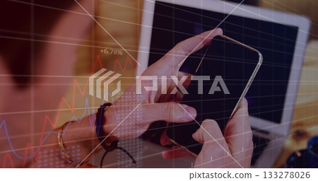 Holding smartphone above office desk wearing bracelet and bangle, with laptop and overlaid charts Holding smartphone above office desk wearing bracelet and bangle, with laptop and overlaid charts 133278026