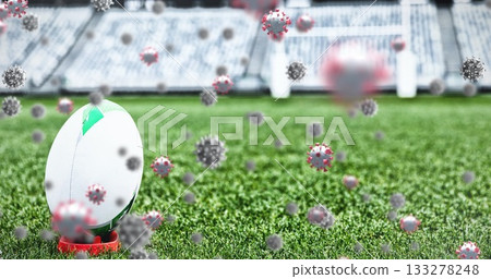 Resting rugby ball on red kicking tee at stadium pitch with floating coronavirus models, copy space 133278248