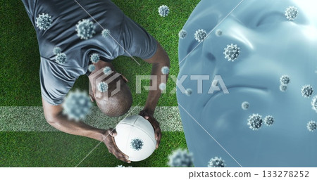 Gripping rugby ball athlete in sportswear crouching on field, with virus, head overlay, copy space 133278252
