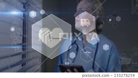 Holding tablet, scrub nurse analyzing beside blinds in corridor, with stethoscope and health icons Holding tablet, scrub nurse analyzing beside blinds in corridor, with stethoscope and health icons 133278259
