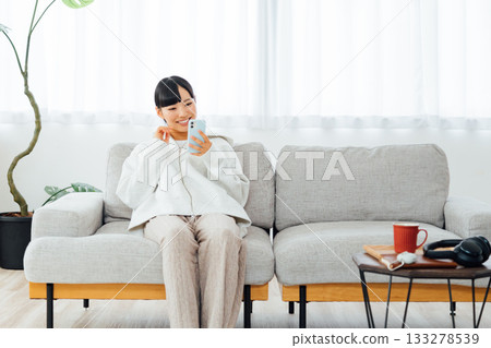 A woman relaxing in her room and using her smartphone A woman relaxing in her room and using her smartphone 133278539