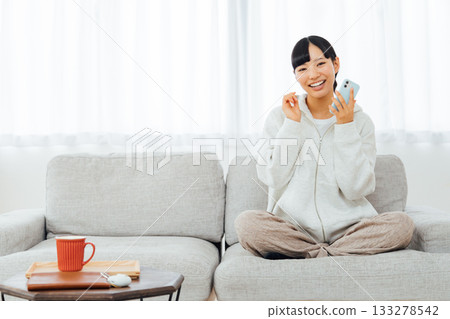 A woman relaxing in her room and using her smartphone A woman relaxing in her room and using her smartphone 133278542