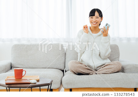 一位女士在房間放鬆地使用智慧型手機 一位女士在房間放鬆地使用智慧型手機 133278543