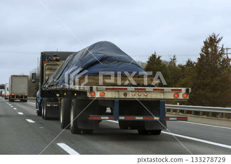 Large truck carries load covered with blue tarp on busy highway, surrounded by overcast Large truck carries load covered with blue tarp on busy highway, surrounded by overcast 133278729