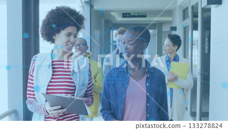Walking colleagues discussing clipboard, holding yellow folder and using earbuds in bright corridor 133278824