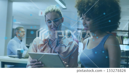 Examining co-workers leaning over tablet in office, man typing laptop with coffee, padlock graphic 133278826