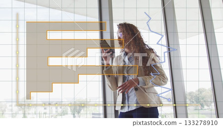 Standing woman in beige blazer reviewing smartphone data by office windows, financial chart overlay Standing woman in beige blazer reviewing smartphone data by office windows, financial chart overlay 133278910