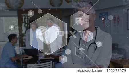 Standing senior female physician crossing arms in clinic room, with laptop charts and medical icons Standing senior female physician crossing arms in clinic room, with laptop charts and medical icons 133278979