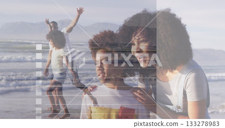 Gazing mother and daughter kneeling near shoreline, with father and son stepping through surf 133278983