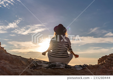 Meditation sunset silhouette woman practicing yoga pose on rocky cliff with peaceful expansive sky 133280444