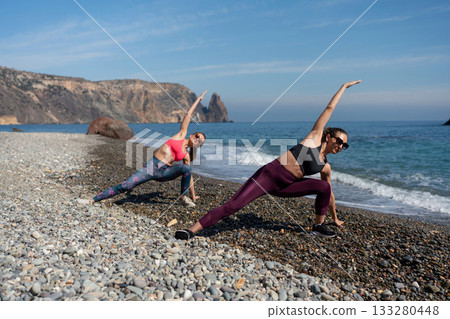 Yoga women stretching fitness exercise routine on remote pebble beach cliffside Yoga women stretching fitness exercise routine on remote pebble beach cliffside 133280448