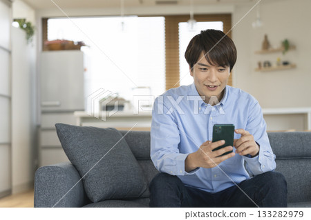 A man in his 30s operating a smartphone in the living room at home 133282979
