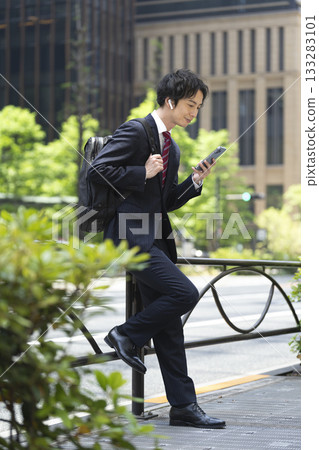 A businessman in his 30s wearing earphones looking at his smartphone screen 133283101