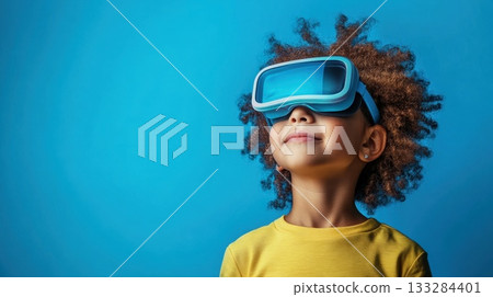 Child exploring virtual reality technology while wearing a headset against a vibrant blue background 133284401