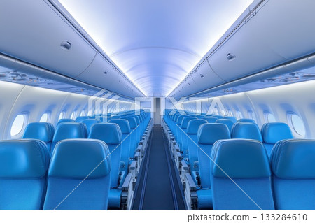 Interior view of a modern airplane cabin showing empty blue seats and ambient lighting in a spacious layout during a daytime flight 133284610