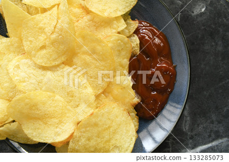 Potato crisps or potato chips with tomato ketchup on a plate. Potato crisps or potato chips with tomato ketchup on a plate. 133285073