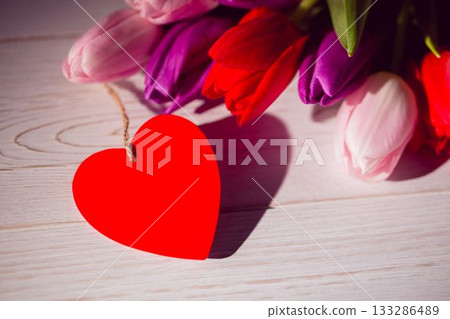 Flat design showing red heart-shaped twine-tied tag on whitewashed tabletop with colorful tulips 133286489