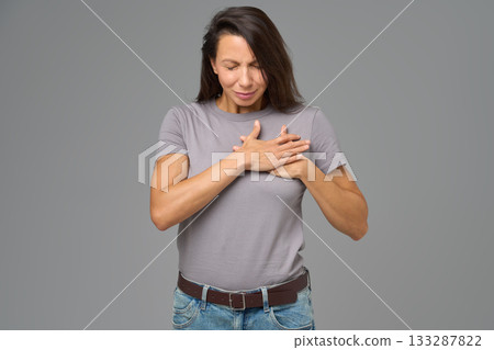 Woman holding chest with both hands and eyes closed in discomfort, studio shot Woman holding chest with both hands and eyes closed in discomfort, studio shot 133287822