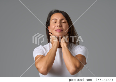 Calm woman closing eyes and holding neck gently expressing relief and relaxation Calm woman closing eyes and holding neck gently expressing relief and relaxation 133287823