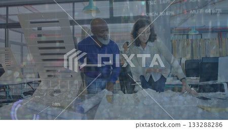 Leaning architects reviewing blueprints on table in modern office, with laptops and documents 133288286