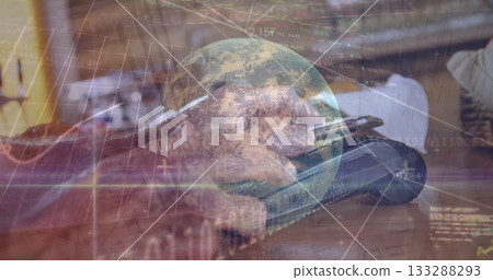 Senior wearing sweater tapping smartphone on wooden desk, with coffee cup, laptop, globe and charts 133288293