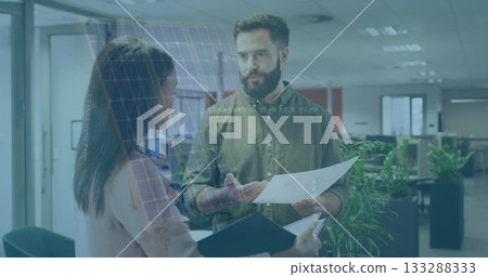 Two colleagues wearing office attire reviewing documents in open plan office, with paper and binder 133288333