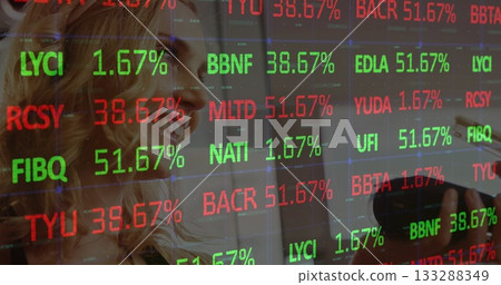 Two colleagues in business attire analyzing stock tickers on digital screen in office, with stylus 133288349