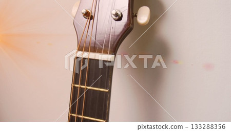 Showing acoustic guitar headstock leaning against wall, with tuning pegs, strings and lens flare 133288356