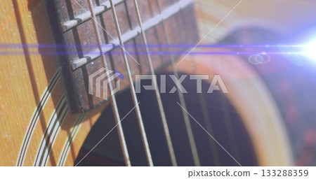 Displaying acoustic guitar with metal strings running across fretboard in studio, with lens flare 133288359