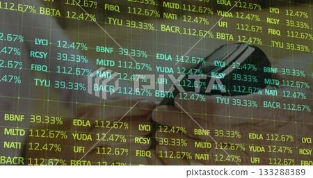 Showing hand holding smartphone above laptop keys with mug on desk, featuring stock ticker overlay 133288389