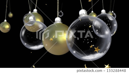 Hanging clear glass and gold baubles in dark studio on cords with caps, drifting star confetti Hanging clear glass and gold baubles in dark studio on cords with caps, drifting star confetti 133288448