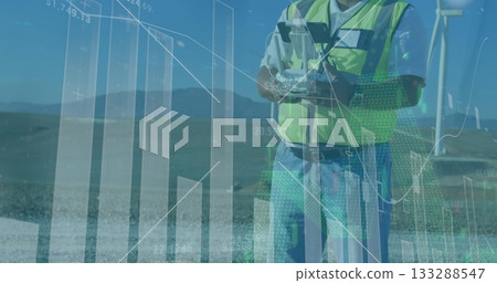 Operating technician wearing safety vest using joystick remote at wind turbine site, showing charts 133288547