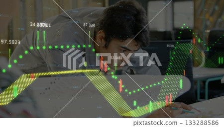 Leaning office worker wearing grey shirt writing papers at office desk, with pencil, stock charts Leaning office worker wearing grey shirt writing papers at office desk, with pencil, stock charts 133288586