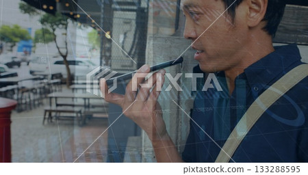 Leaning Asian man wearing shoulder bag holding smartphone on city sidewalk, copy space Leaning Asian man wearing shoulder bag holding smartphone on city sidewalk, copy space 133288595