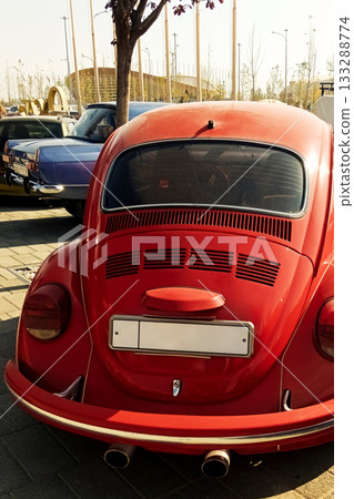 a rear view of a red classic small car with a rounded body and twin exhaust pipes 133288774