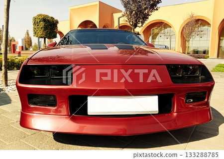 the front of a red sports coupe at an exhibition with an orange building in the background the front of a red sports coupe at an exhibition with an orange building in the background 133288785