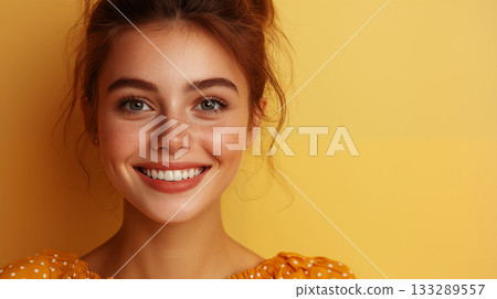Young woman smiling naturally against vibrant yellow background closeup 133289557