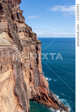 Vertical view of Sao Lourenco cliff with layered rock descending steeply to clear sea waves 133290391