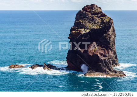 Volcanic sea stack off Sao Lourenco rises from deep blue Atlantic with waves and sunlit texture 133290392