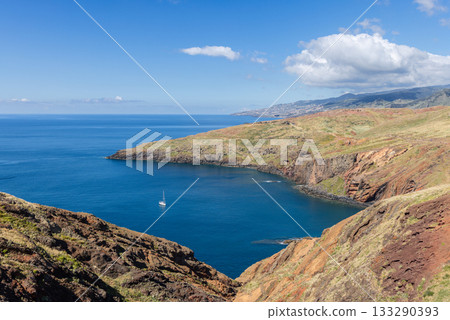 White sailboat rests in Sao Lourenco bay framed by volcanic cliffs and green grassy slopes 133290393