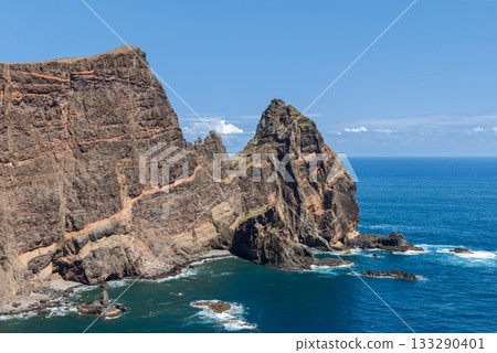 Striped volcanic cliffs of Sao Lourenco plunge into calm deep blue Atlantic with rich textures 133290401